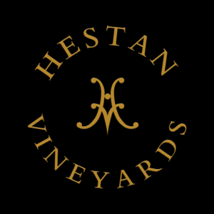 Gold Hestan Vineyards text forms a circle around a stylized H logo, all set against a striking black background.